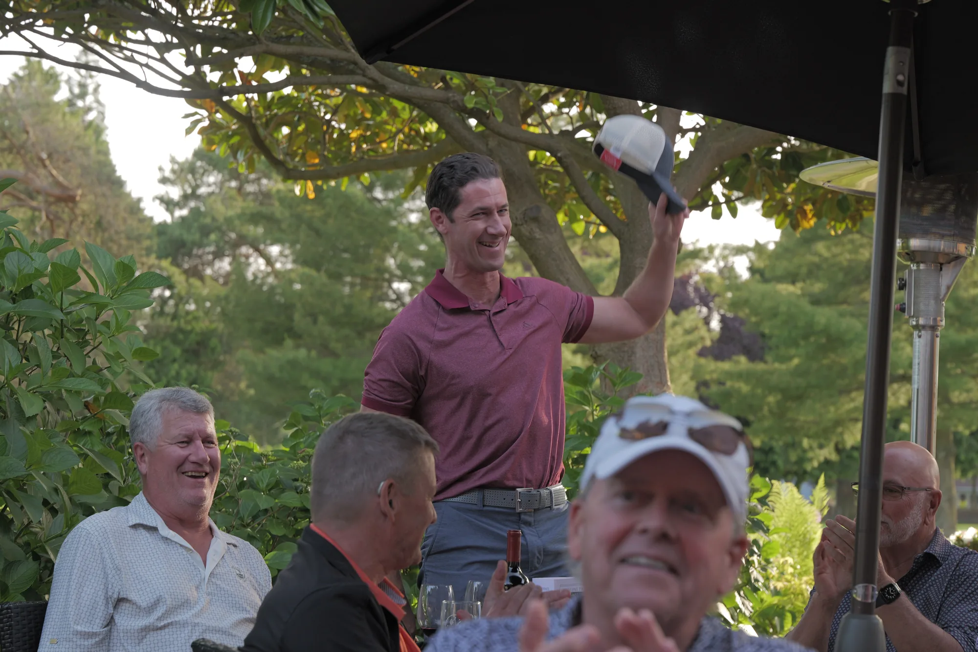 A member raises his cap to cheers from his table on the Beach Grove Golf Club patio